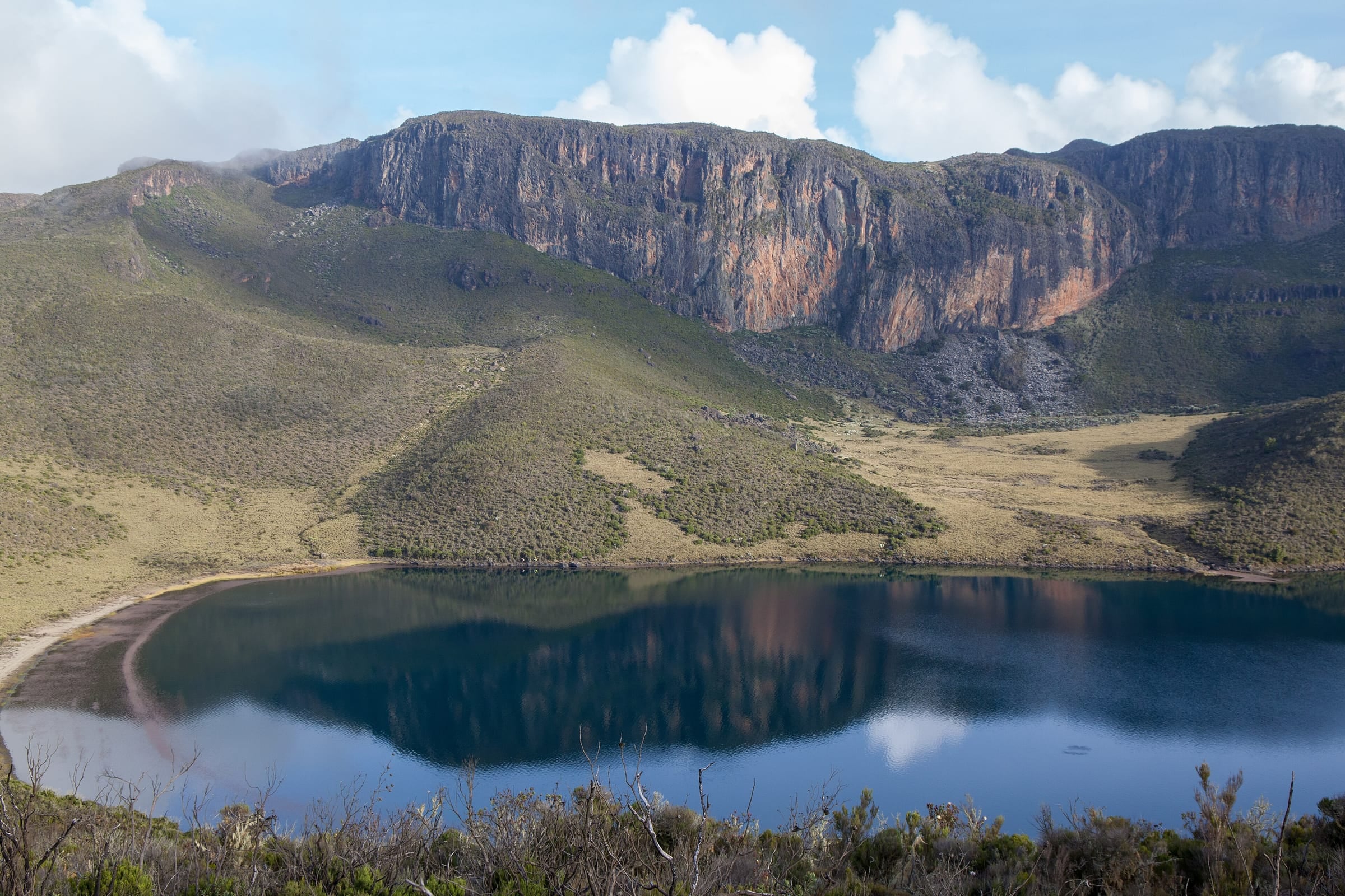 Lake Alice reflecting the bare rock cliffs of its crater on Mt. Kenya